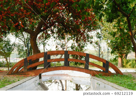 A small arch bridge over decorated canal pond in garden park city surrounded by maple tree canopy A small arch bridge over decorated canal pond in garden park city surrounded by maple tree canopy 69212119