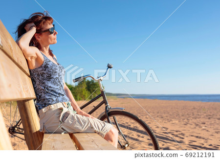 Middle-aged woman came on a Bicycle to the beach and resting sit Middle-aged woman came on a Bicycle to the beach and resting sit 69212191