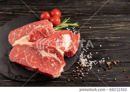 Three pieces of juicy raw beef on a stone cutting board on a black wooden table background. Three pieces of juicy raw beef on a stone cutting board on a black wooden table background. 69212302