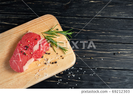 one pieces of juicy raw beef on a cutting board on a black wooden table background. one pieces of juicy raw beef on a cutting board on a black wooden table background. 69212303