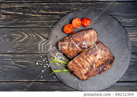 juicy piece of fried meat lies on a stone plate against a black wooden table juicy piece of fried meat lies on a stone plate against a black wooden table 69212304