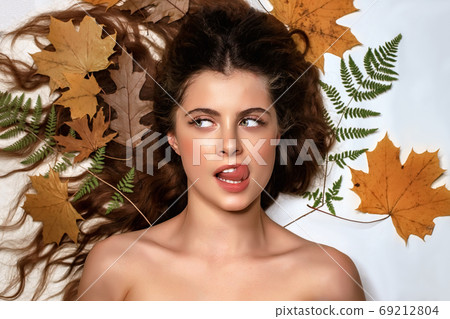 Portrait of a young brunette woman on a white background with a green fern and yellow leaves around her head 69212804