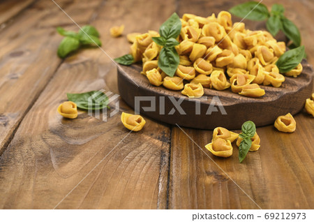 Tortellini mignon on a wooden board with basil and parmesan. Specialties of the cuisine from Bologna Tortellini mignon on a wooden board with basil and parmesan. Specialties of the cuisine from Bologna 69212973