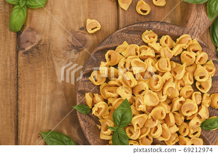 Tortellini mignon on a wooden board with basil and parmesan. Specialties of the cuisine from Bologna Tortellini mignon on a wooden board with basil and parmesan. Specialties of the cuisine from Bologna 69212974