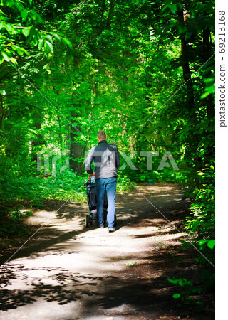 Forest dirty road and walking man with baby carriage in a sunny summer day. Forest dirty road and walking man with baby carriage in a sunny summer day. 69213168