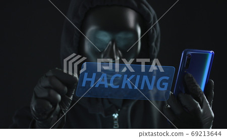 Hacker wearing black mask pulls HACKING tab from a smartphone Hacker wearing black mask pulls HACKING tab from a smartphone 69213644