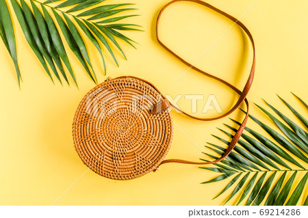 Fashionable handmade natural round rattan bag and tropical leaves on yellow background.  69214286