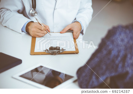 Unknown red-bearded doctor and patient woman discussing current health examination while sitting in sunny clinic, close-up. Medicine concept 69214287