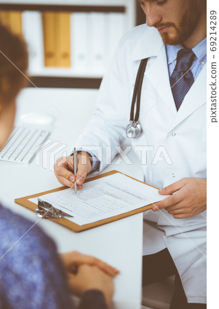 Unknown red-bearded doctor and patient woman discussing current health examination while sitting in sunny clinic, close-up. Medicine concept 69214289