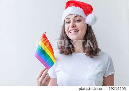 Beautiful lesbian girl in red Santa Claus hat with LGBT rainbow flag isolated on white background looking happy and excited. Young woman Gay Pride portrait. Happy Christmas and New Year holidays Beautiful lesbian girl in red Santa Claus hat with LGBT rainbow flag isolated on white background looking happy and excited. Young woman Gay Pride portrait. Happy Christmas and New Year holidays 69214293