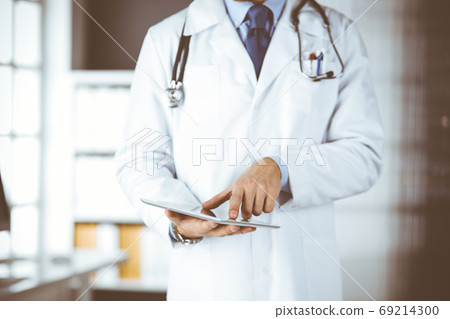 Male doctor using tablet computer in clinic, close-up. Perfect medical service in hospital. Medicine and healthcare concept Male doctor using tablet computer in clinic, close-up. Perfect medical service in hospital. Medicine and healthcare concept 69214300