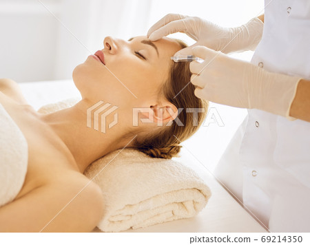 Beautiful woman receiving beauty injections with closed eyes. Beautician doctor hands doing beauty procedure to female face with syringe 69214350