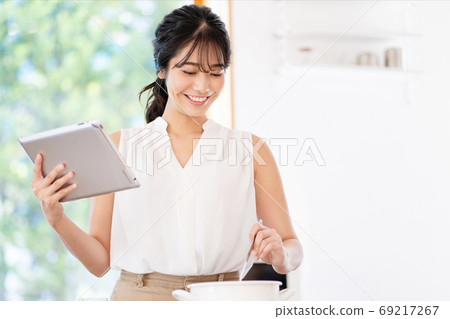 使用片劑的一名婦女在廚房裡 使用片劑的一名婦女在廚房裡 69217267
