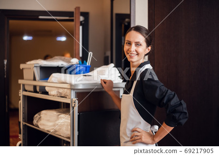A smiling hotel maid with cleaning cart and cleaning supplies, l 69217905