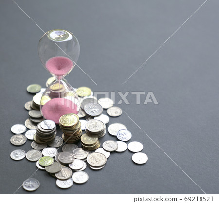 Hourglass with sand flowing and coins on table. Hourglass with sand flowing and coins on table. 69218521