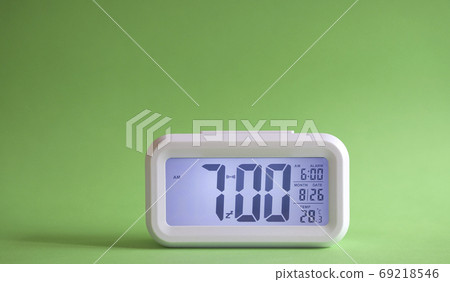 Digital alarm clock on table with green background. Digital alarm clock on table with green background. 69218546