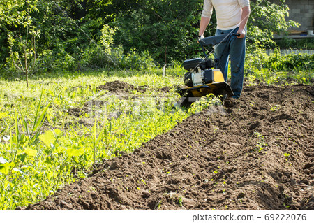 Perspective view of man plowing soil by motor cultivator 69222076
