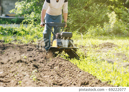 Perspective view of man plowing raw in soil by motor cultivator Perspective view of man plowing raw in soil by motor cultivator 69222077