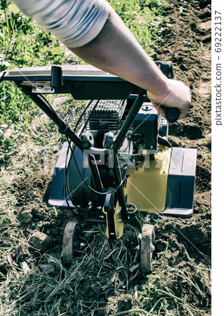 A motor cultivator plowing a raw in soil vertical A motor cultivator plowing a raw in soil vertical 69222137