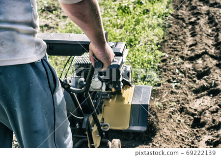 A motor cultivator plowing a raw in gerden soil A motor cultivator plowing a raw in gerden soil 69222139