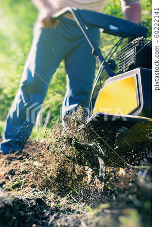 The man tills the soil with the motor cultivator The man tills the soil with the motor cultivator 69222141