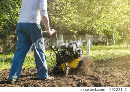A man plowing a soil by motor cultivator perspective view A man plowing a soil by motor cultivator perspective view 69222142