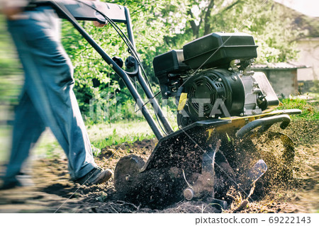 A man plowing a soil by motor cultivator outdoor garden work A man plowing a soil by motor cultivator outdoor garden work 69222143