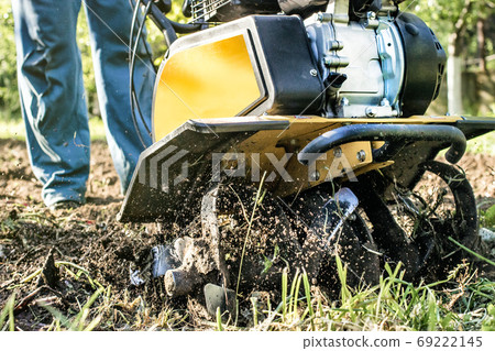 A man plowing a garden soil by motor cultivator bottom view A man plowing a garden soil by motor cultivator bottom view 69222145