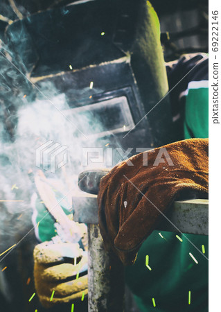 A man in weld mask with electric weld in his hand welding a metal frame A man in weld mask with electric weld in his hand welding a metal frame 69222146