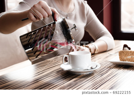 The girl pours tea in a cup from the French press in cafe, nature light The girl pours tea in a cup from the French press in cafe, nature light 69222155