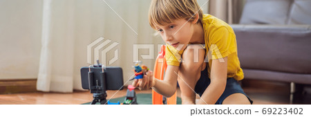 BANNER, LONG FORMAT Staying connected. Happy young boy looking at his mobile phone and smiling while playing with toys. A boy talks to someone via video communication during self-isolation due to 69223402