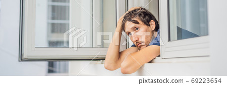 BANNER, LONG FORMAT Extremly tired young man looking out the window, home alone. self-isolation at home, quarantine due to pandemic COVID 19. Mental health problems in self-isolation at home 69223654