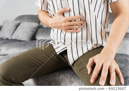 Young man suffering from abdominal pain while sitting on sofa at home. Young man suffering from abdominal pain while sitting on sofa at home. 69223687