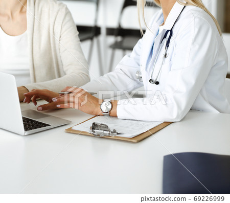 Unknown woman-doctor sitting and communicating with female patient. Physician checks medical history record and exam results, close-up. Healthcare concept Unknown woman-doctor sitting and communicating with female patient. Physician checks medical history record and exam results, close-up. Healthcare concept 69226999