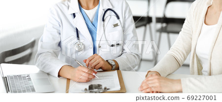 Unknown woman-doctor sitting and communicating with female patient. Physician checks medical history record and exam results, close-up. Healthcare concept Unknown woman-doctor sitting and communicating with female patient. Physician checks medical history record and exam results, close-up. Healthcare concept 69227001