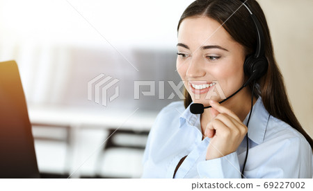 Brunette female customer service representative using headset and consulting clients online. Call center Brunette female customer service representative using headset and consulting clients online. Call center 69227002