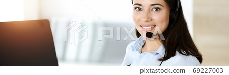 Brunette female customer service representative using headset and consulting clients online. Call center Brunette female customer service representative using headset and consulting clients online. Call center 69227003