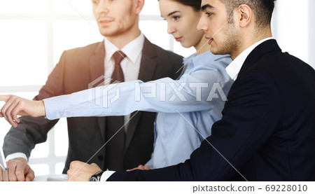 Group of business people discussing questions at meeting in sunny office. Colleagues working with computer 69228010