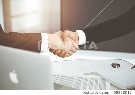 Unknown diverse business people are shaking hands finishing contract signing in sunny office, close-up. Business handshake concept Unknown diverse business people are shaking hands finishing contract signing in sunny office, close-up. Business handshake concept 69228012