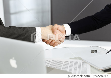 Unknown diverse business people are shaking hands finishing up meeting at the desk in office, close-up. Handshake concept Unknown diverse business people are shaking hands finishing up meeting at the desk in office, close-up. Handshake concept 69228013