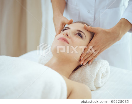 Young and blonde woman enjoying facial massage in spa salon. Beauty concept 69228085