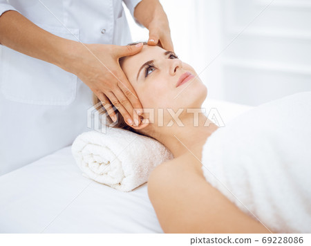 Young and blonde woman enjoying facial massage in spa salon. Beauty concept Young and blonde woman enjoying facial massage in spa salon. Beauty concept 69228086