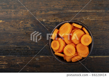 Sliced carrots in a bowl on a wooden background. Vegetable, ingr 69228414