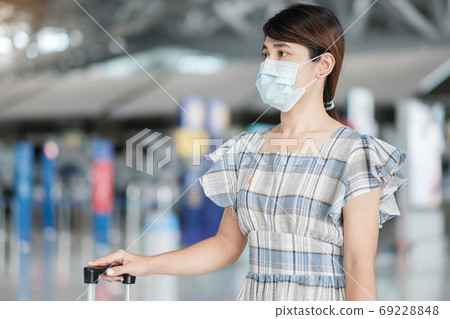 Young female wearing face mask with luggage checking flight time Young female wearing face mask with luggage checking flight time 69228848