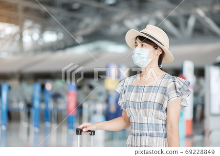 Young female wearing face mask with luggage checking flight time Young female wearing face mask with luggage checking flight time 69228849
