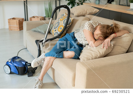 Mature exhausted blond female lying on soft pillows on couch while having rest 69230521
