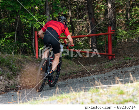 Cyclist goes through open gate bar into terrain in forest. Cyclist goes through open gate bar into terrain in forest. 69230714