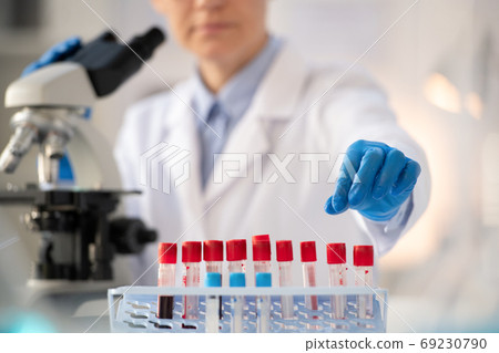 Gloved hand of laboratory worker in whitecoat taking small flask with blood test 69230790