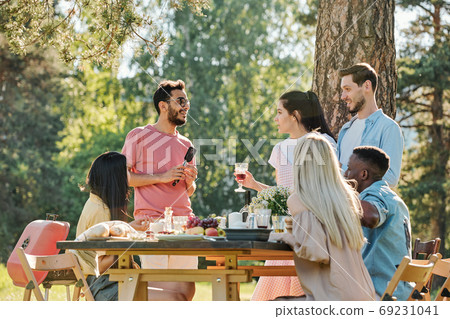 Pretty girl with glass of wine standing by her boyfriend and talking to friend Pretty girl with glass of wine standing by her boyfriend and talking to friend 69231041