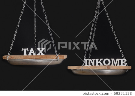 Balance between taxes and income. Balance scales on black background, close up Balance between taxes and income. Balance scales on black background, close up 69231138